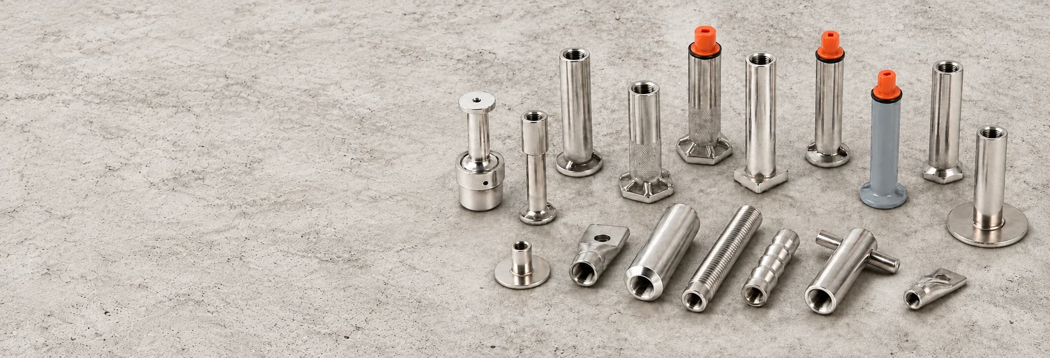 Threaded concrete inserts, hex-foot ferrules, plate-base sockets and cross-pin components grouped on the right of a textured concrete surface