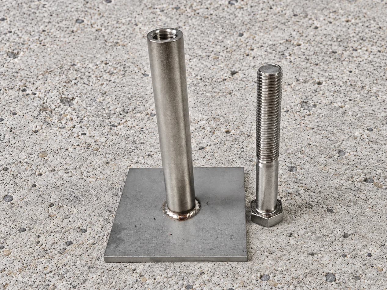 Threaded socket mounted on a square base plate with a separate hex-head bolt beside it